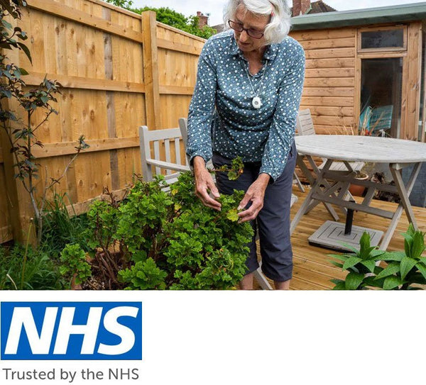 Older lady wearing digital personal alarm neck pendant in garden