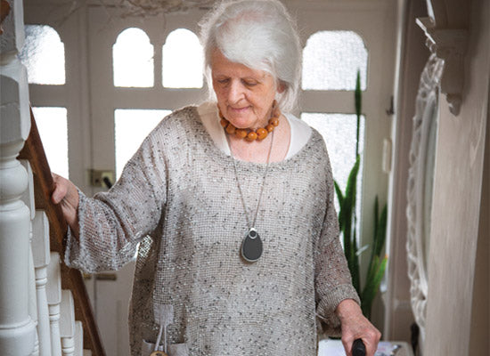 Older person with fall alarm around neck walking up stairs