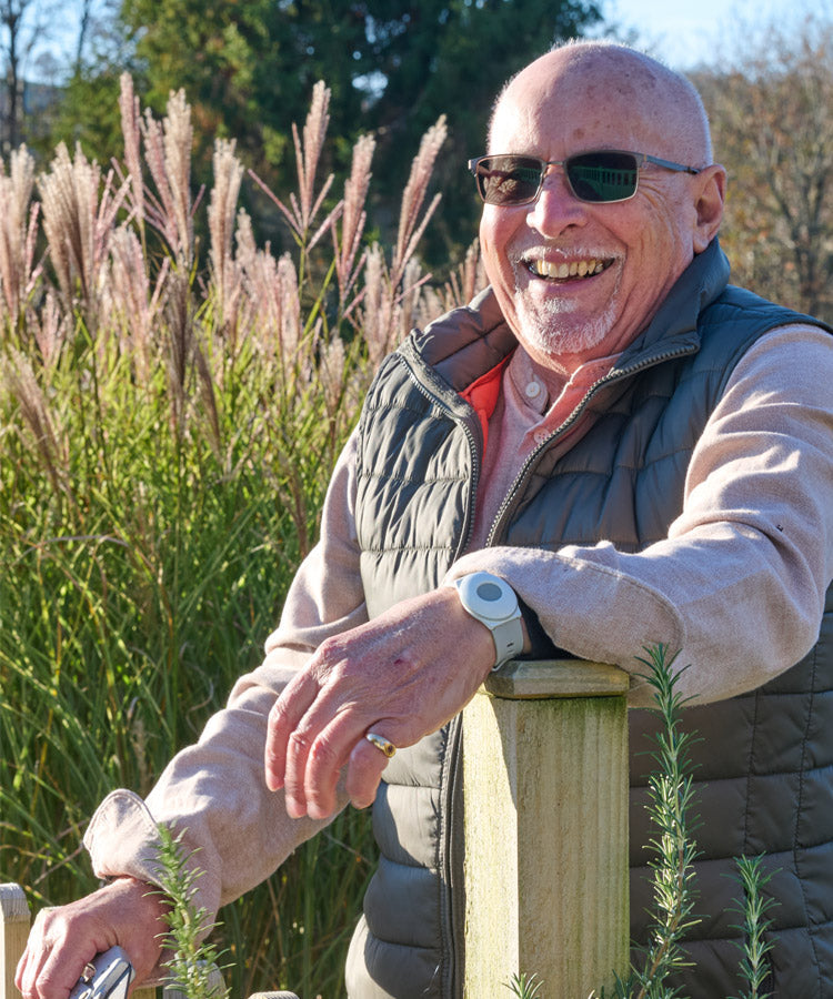 Man wearing sunglasses and a personal alarm standing in front of tall grasses