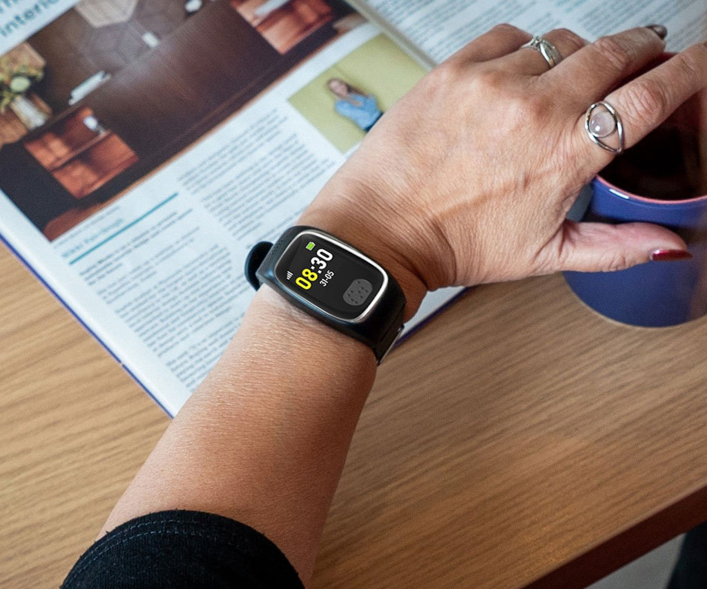 Person wearing a dementia tracker on wrist with a book and mug in the background