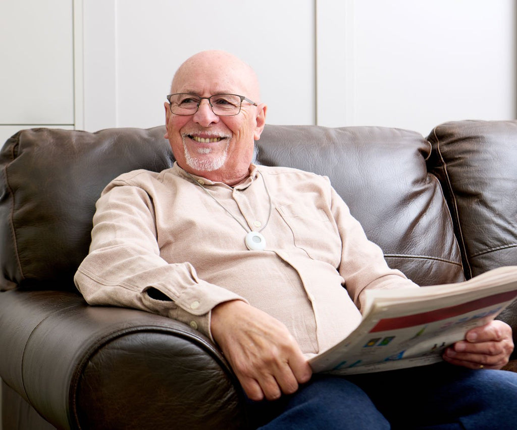 Man sitting on a brown leather couch reading a newspaper.