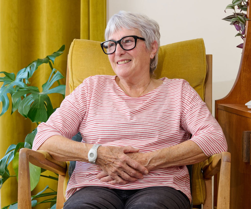 Woman sitting in a yellow chair wearing a pink striped shirt, surrounded by green plants.