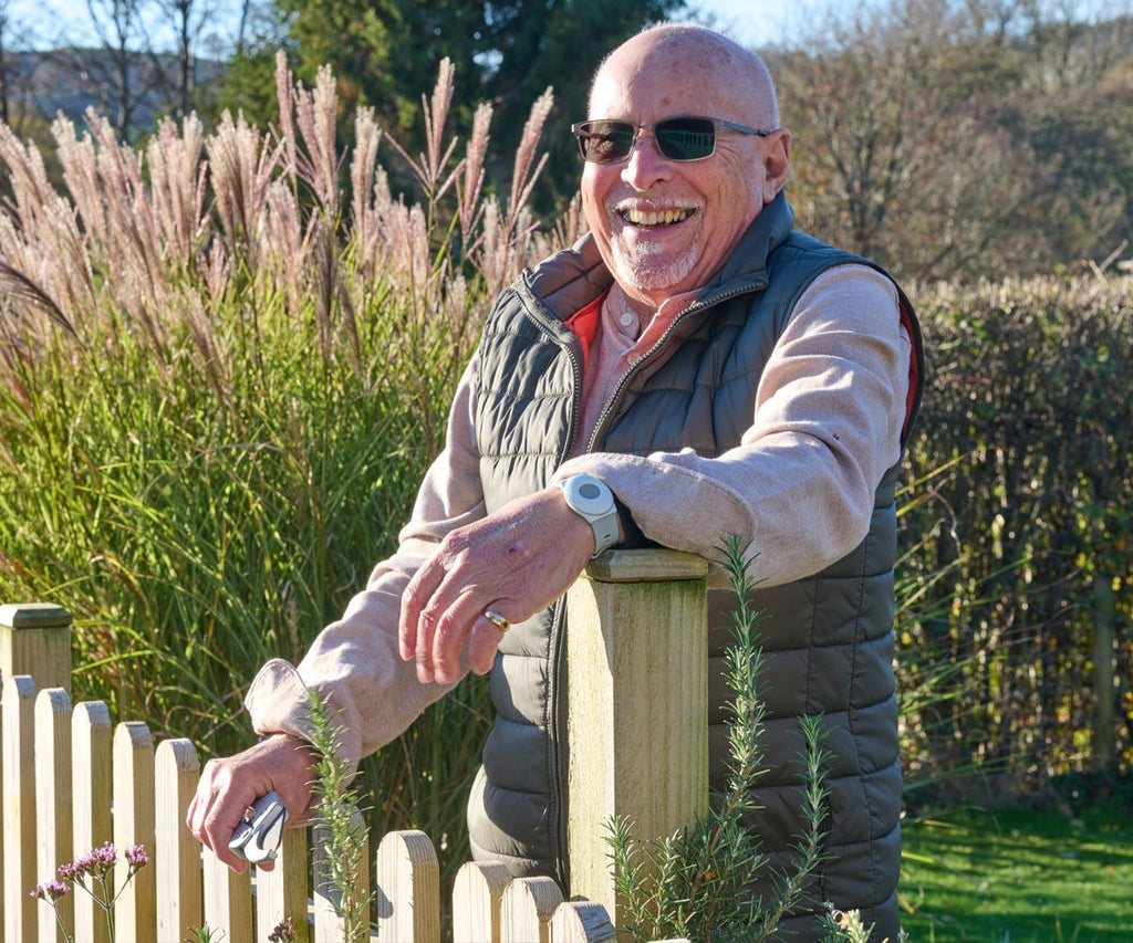 Man standing outdoors with a wooden fence and tall grasses in the background