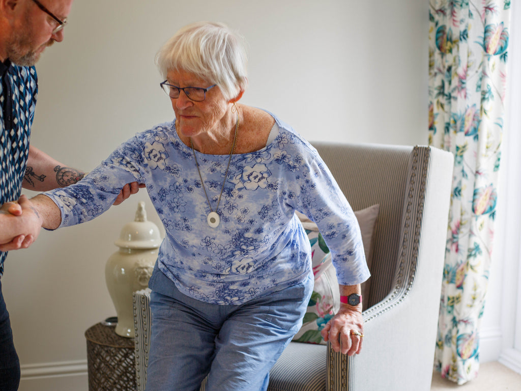 elderly lady wearing personal alarm getting help standing up 