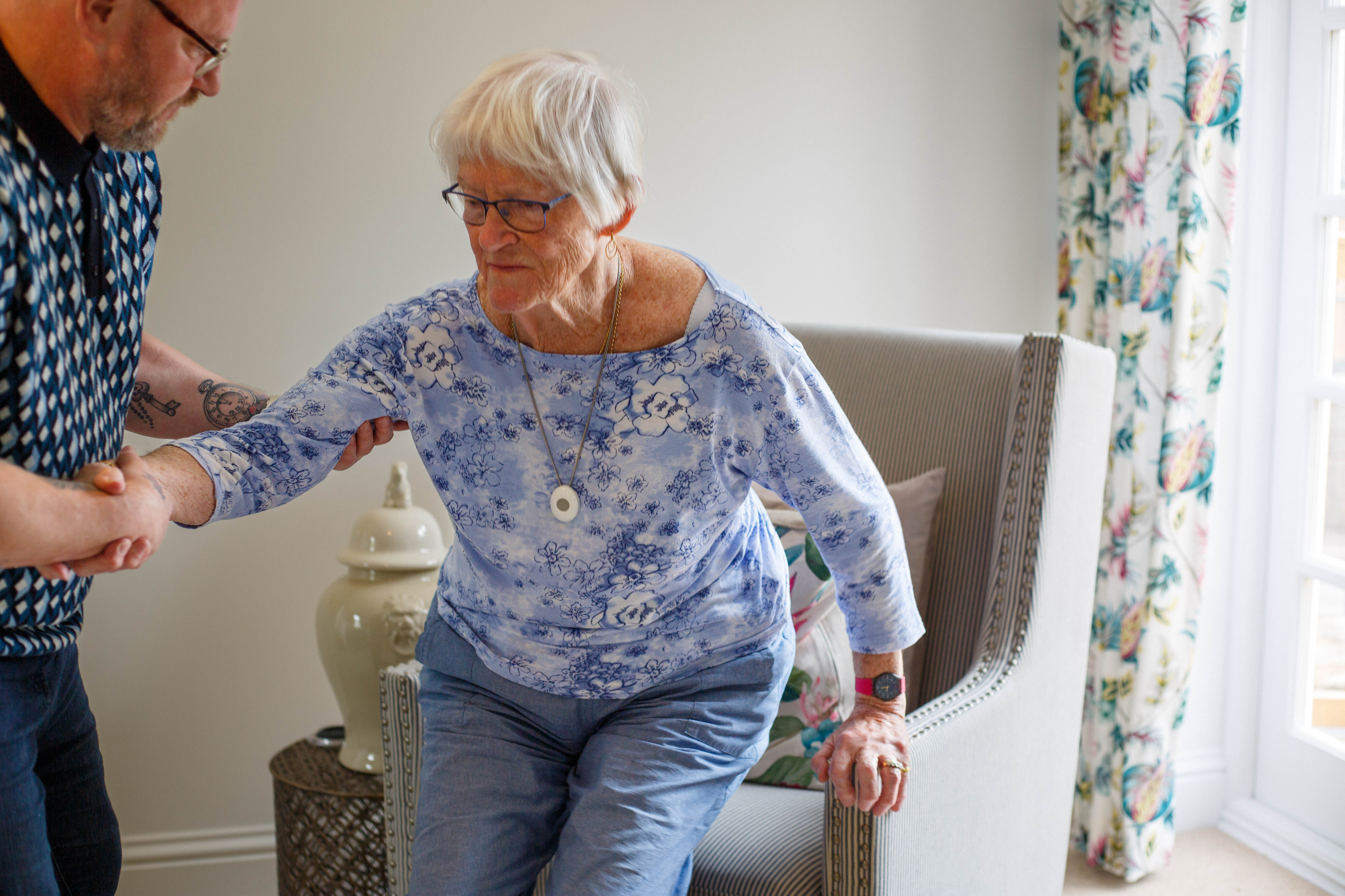 elderly lady wearing personal alarm getting help standing up 