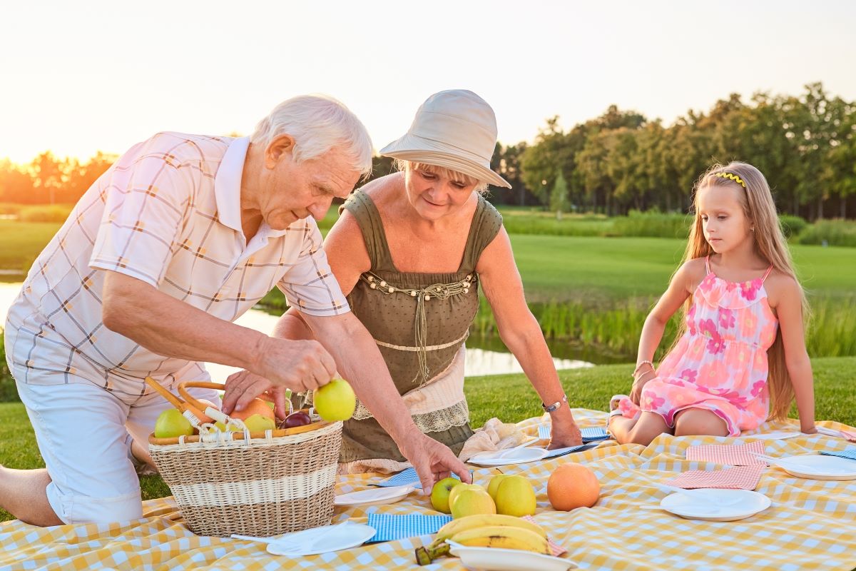 Elderly grandparents having picnic with grandchild in summer