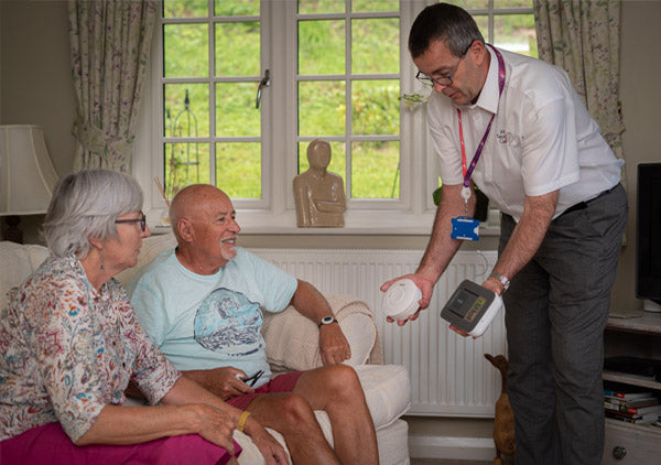 Man demonstrating a device to an elderly couple in a home setting.