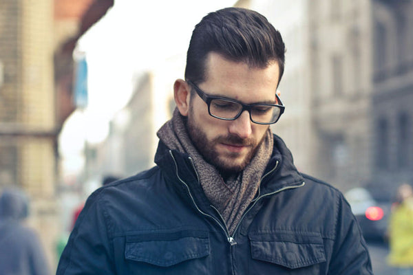 Man wearing glasses and a dark jacket on a city street