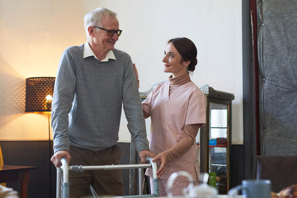 Man using a walker with a caregiver in a home setting
