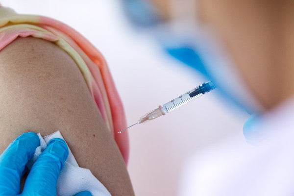 Person receiving an injection with a syringe held by a gloved hand.