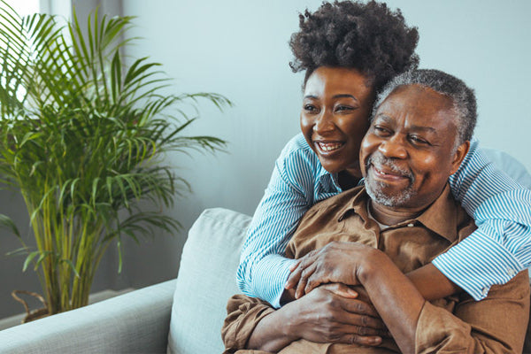 A woman embracing an older man on a couch with a plant in the background