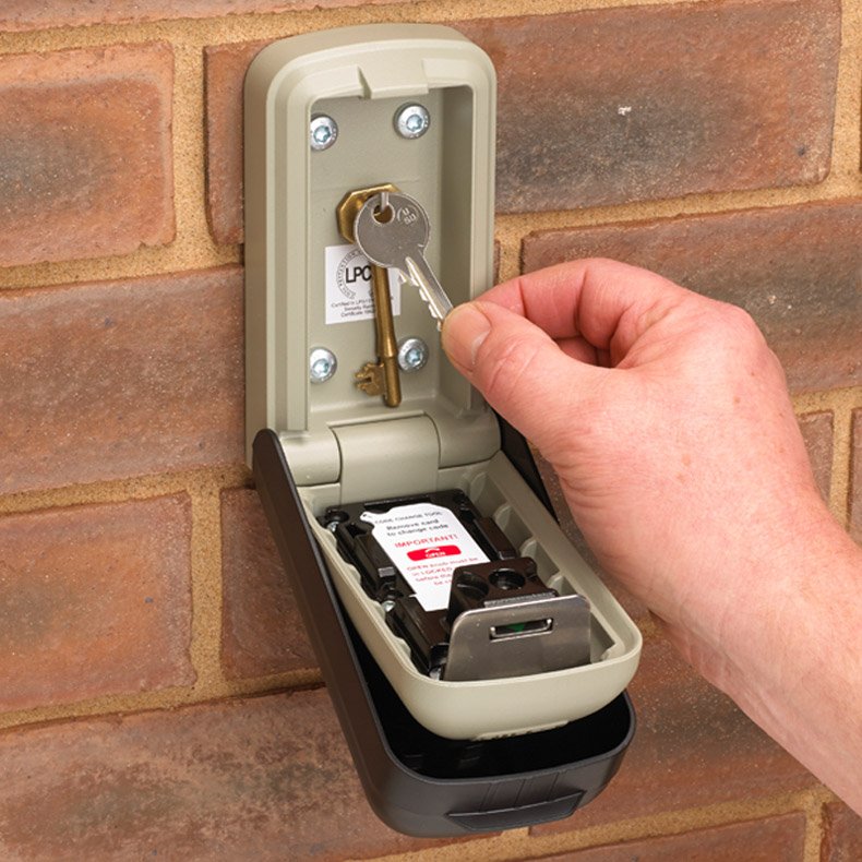 Hand opening a key storage box attached to a brick wall.