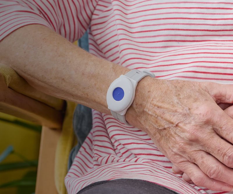 Person wearing a fall alarm with a blue button on an arm in a red and white striped shirt.