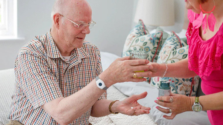 Man receiving a pendant alarm from a woman in a home setting