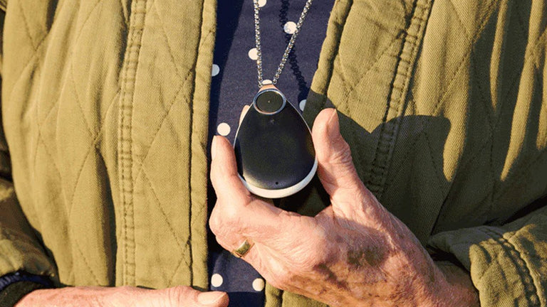 Person holding a alarm pendant, wearing a green jacket.