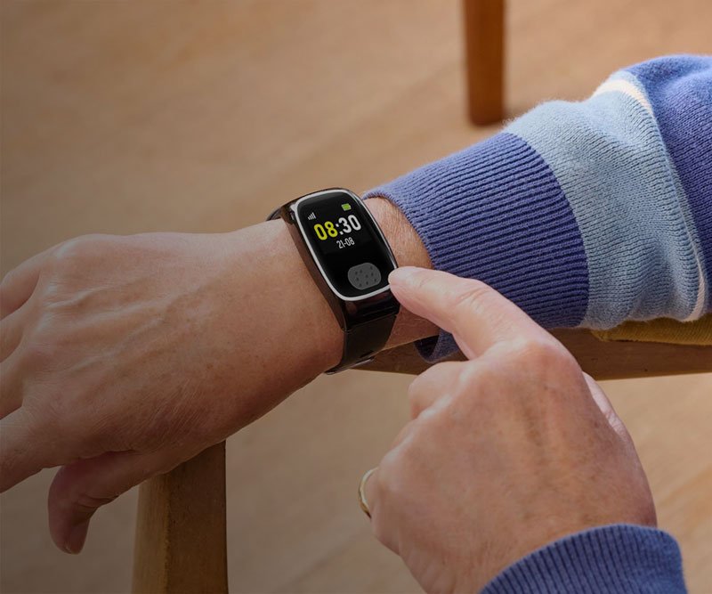 Person adjusting a personal alarm watch on their wrist with a blurred background