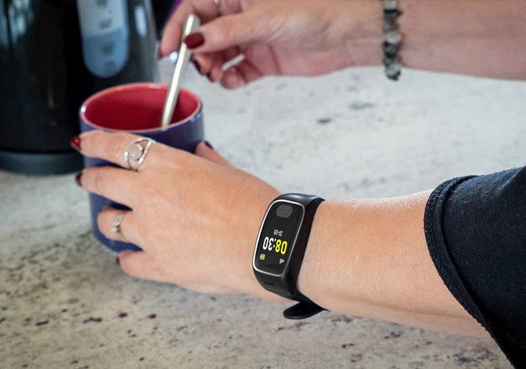 Person holding a mug with a smartwatch displaying time and temperature on a countertop.