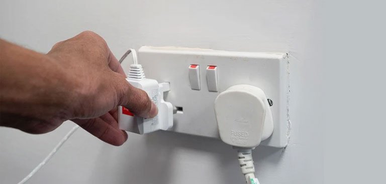 Hand plugging an electrical plug into a wall socket on a light gray background
