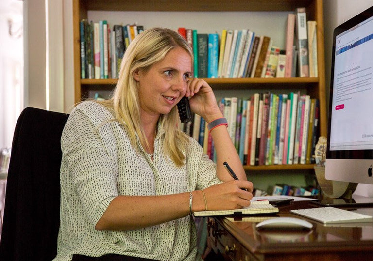 Woman talking on the phone in an office setting with books and a computer in the background