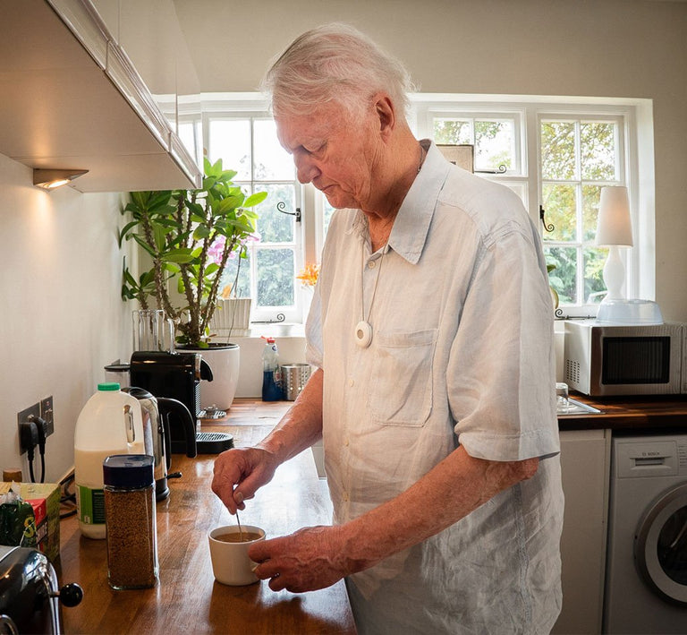 Man stirring a cup in a kitchen wearing an alarm