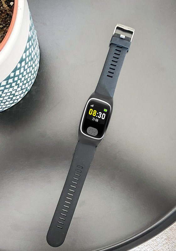 Alarm watch with a gray strap on a reflective surface next to a plant pot.