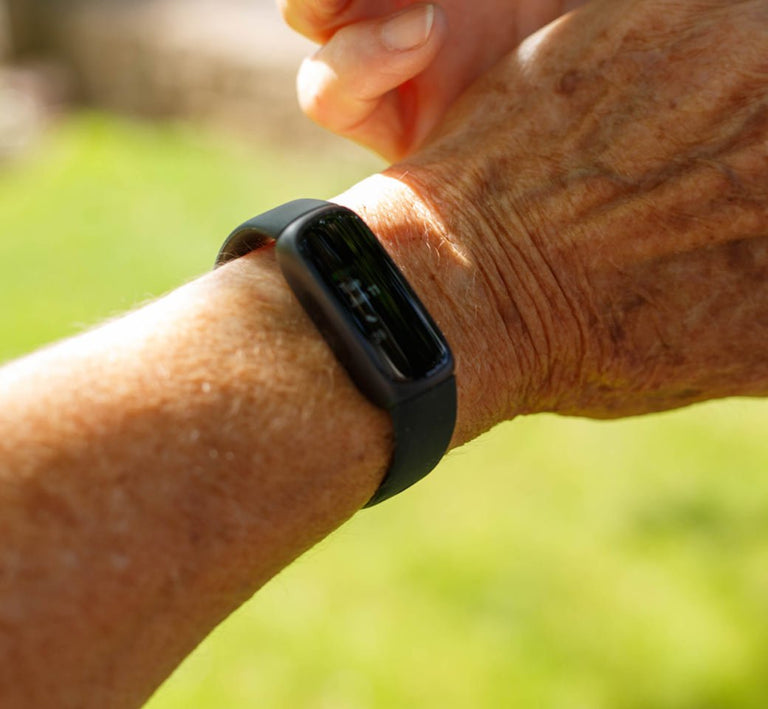 Person wearing a black fitness tracker on a blurred natural background