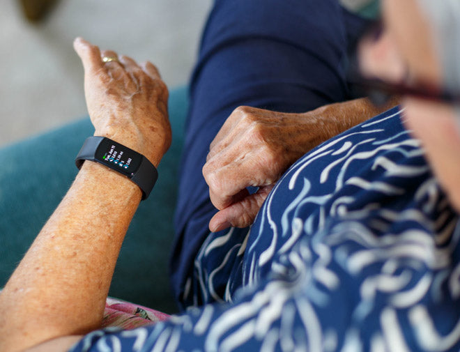 Person wearing a smartwatch with another person holding their hand, possibly in a caregiving context.