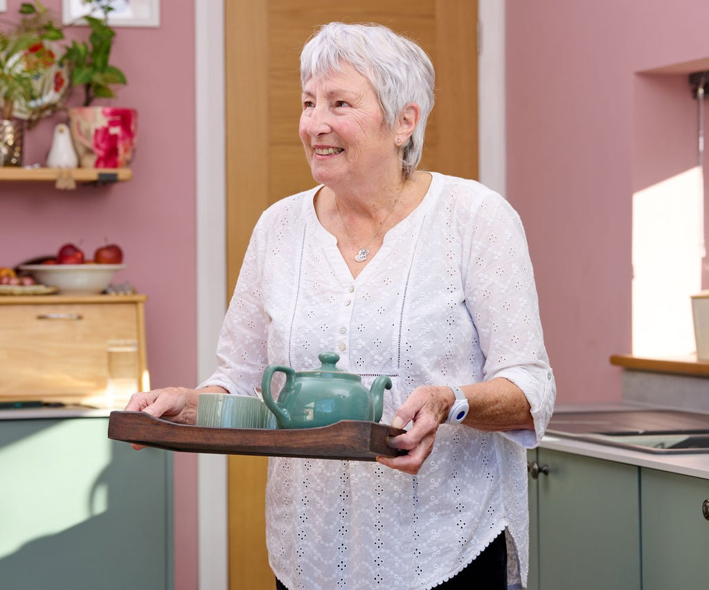 Woman holding a tray with a teapot in a kitchen setting