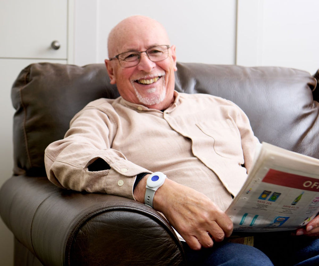 Man sitting on a couch reading a newspaper with a watch on his wrist.