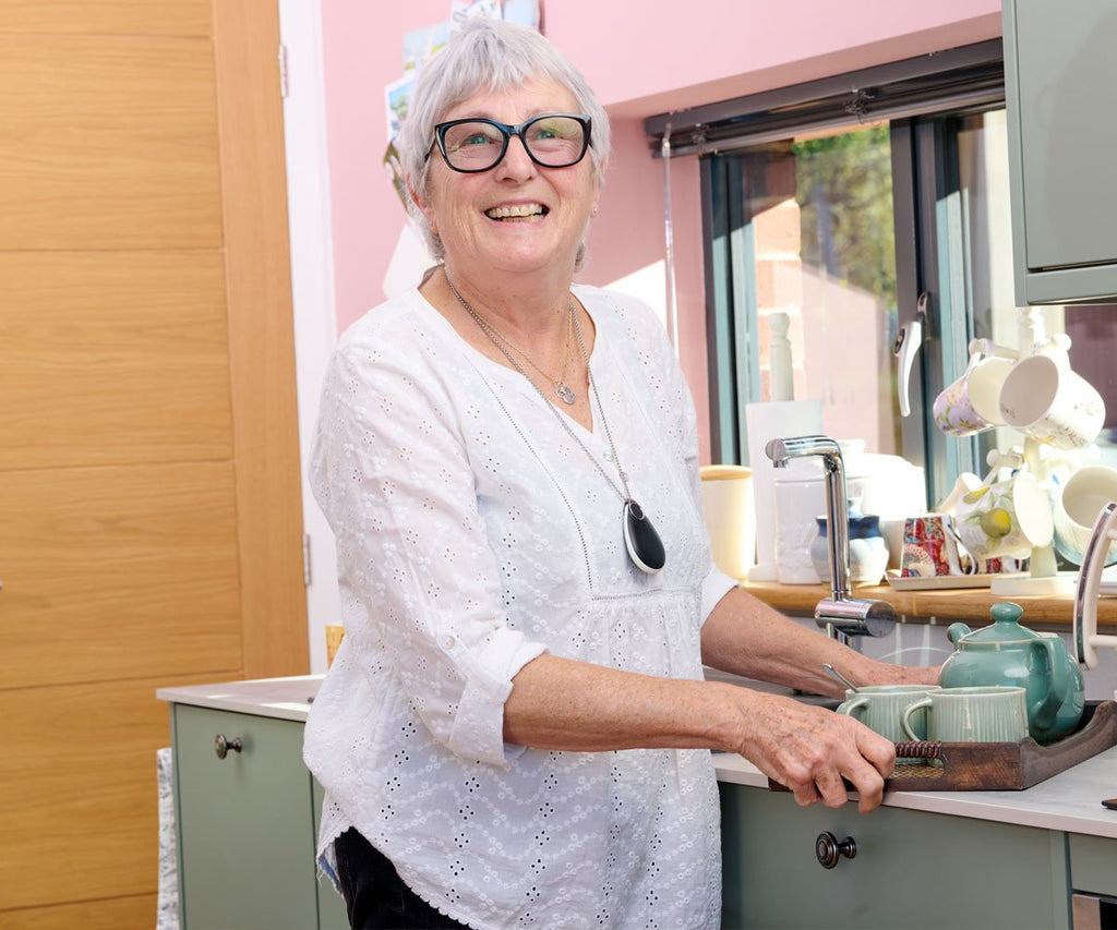 Woman in a kitchen setting with a pink wall and cabinets with neck pendant alarm.