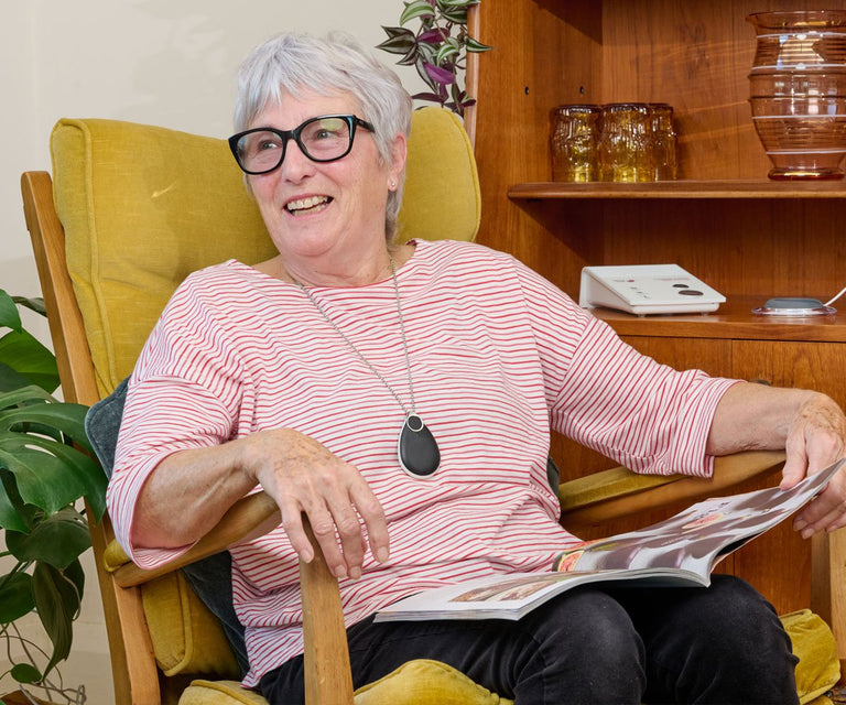 Woman sitting in a chair reading a newspaper, wearing glasses and a pink striped shirt.