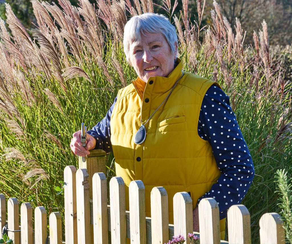 Woman in a yellow vest standing behind a wooden fence with a personal alarm