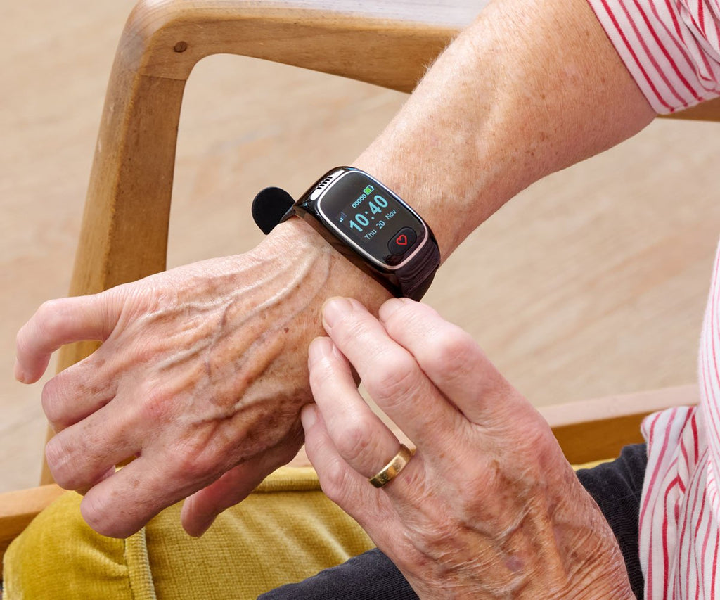 Person wearing a personal alarm watch on an elderly wrist with a blurred background