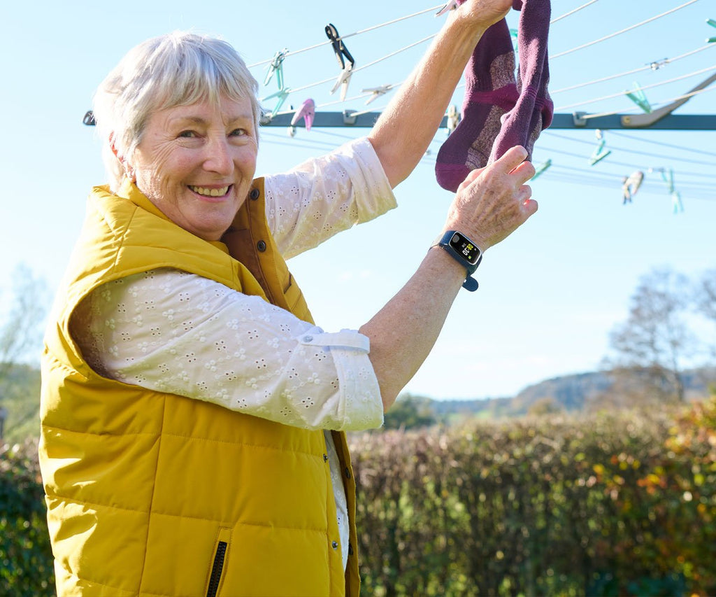 Woman in yellow vest hanging clothes on a line outdoors with a personal alarm watch