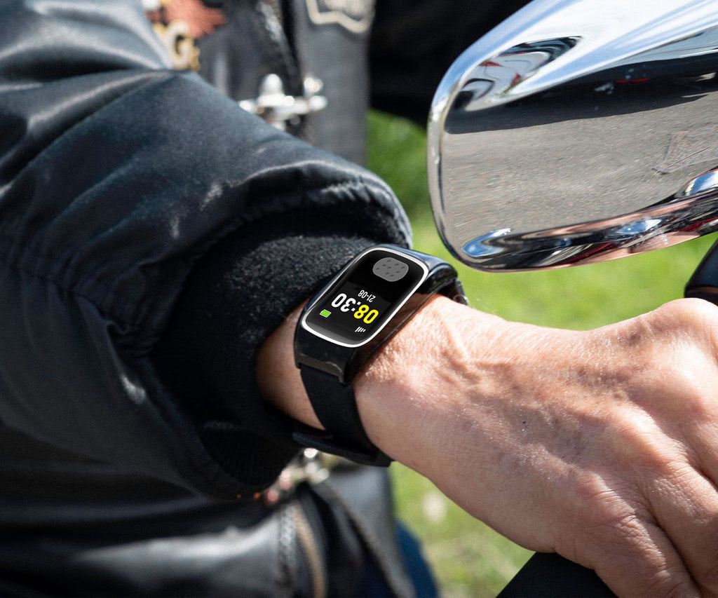 Person wearing a personal alarm watch on a motorcycle with a mirror reflection.