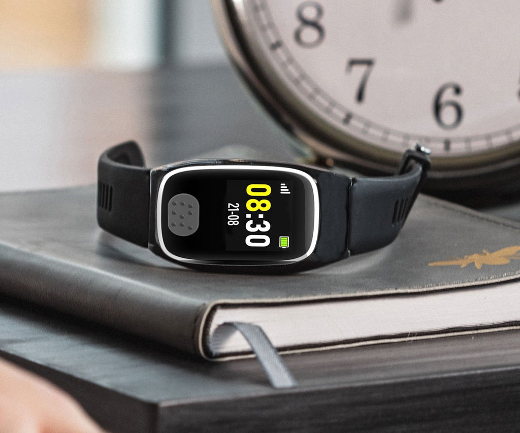 Black personal alarm watch on a notebook with a clock in the background