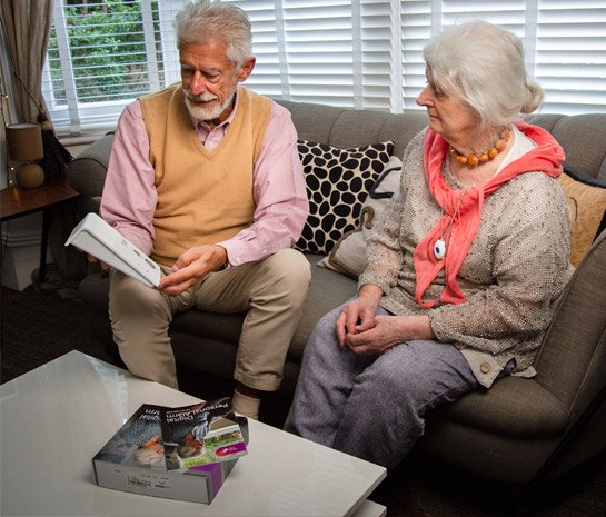 Two elderly people sitting on a couch with a personal alarm
