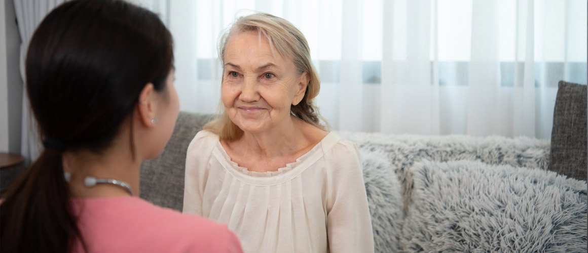Two women sitting on a couch, one of whom is an elderly woman, in a home setting.