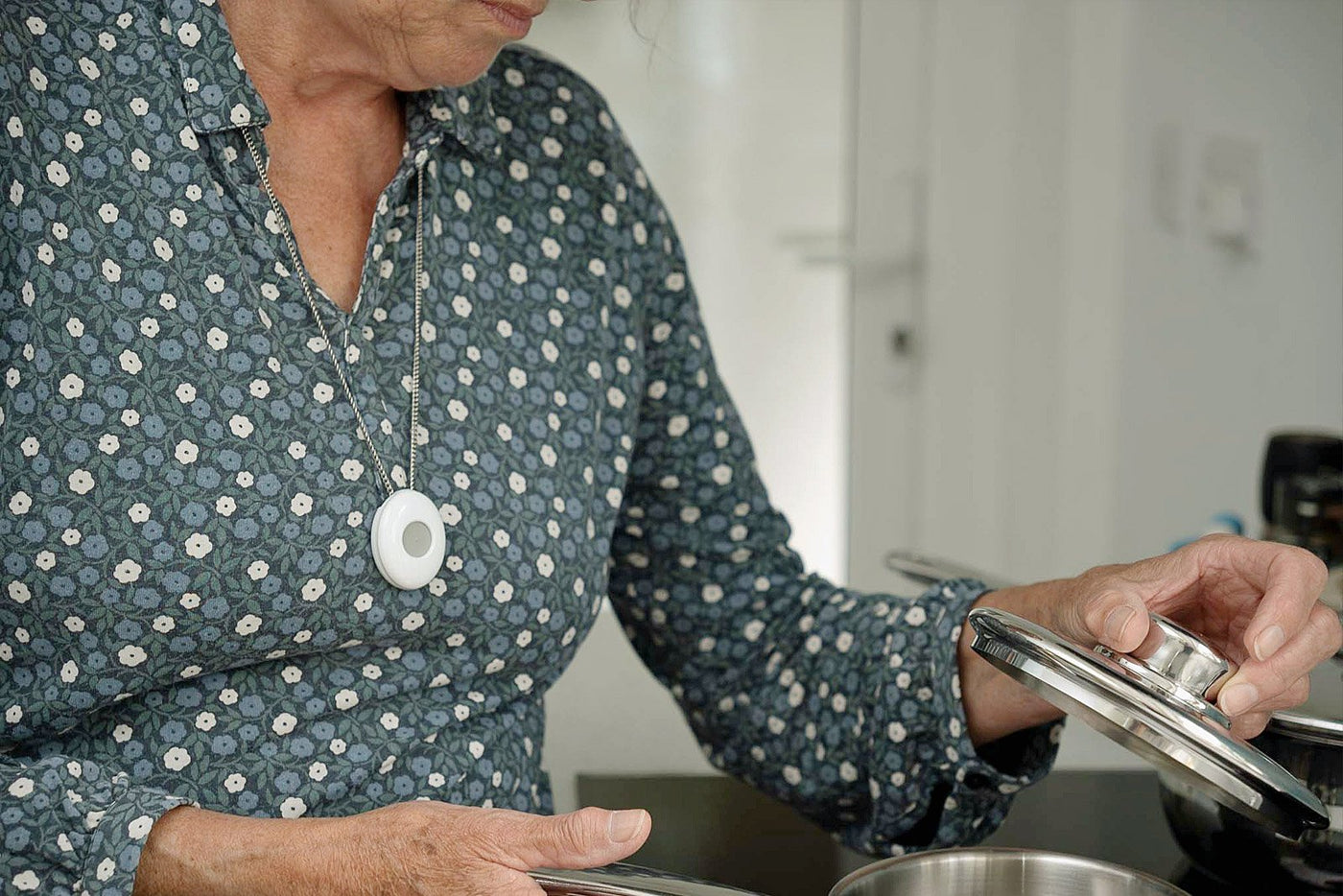 Elderly lady wearing digital personal alarm neck pendant in kitchen