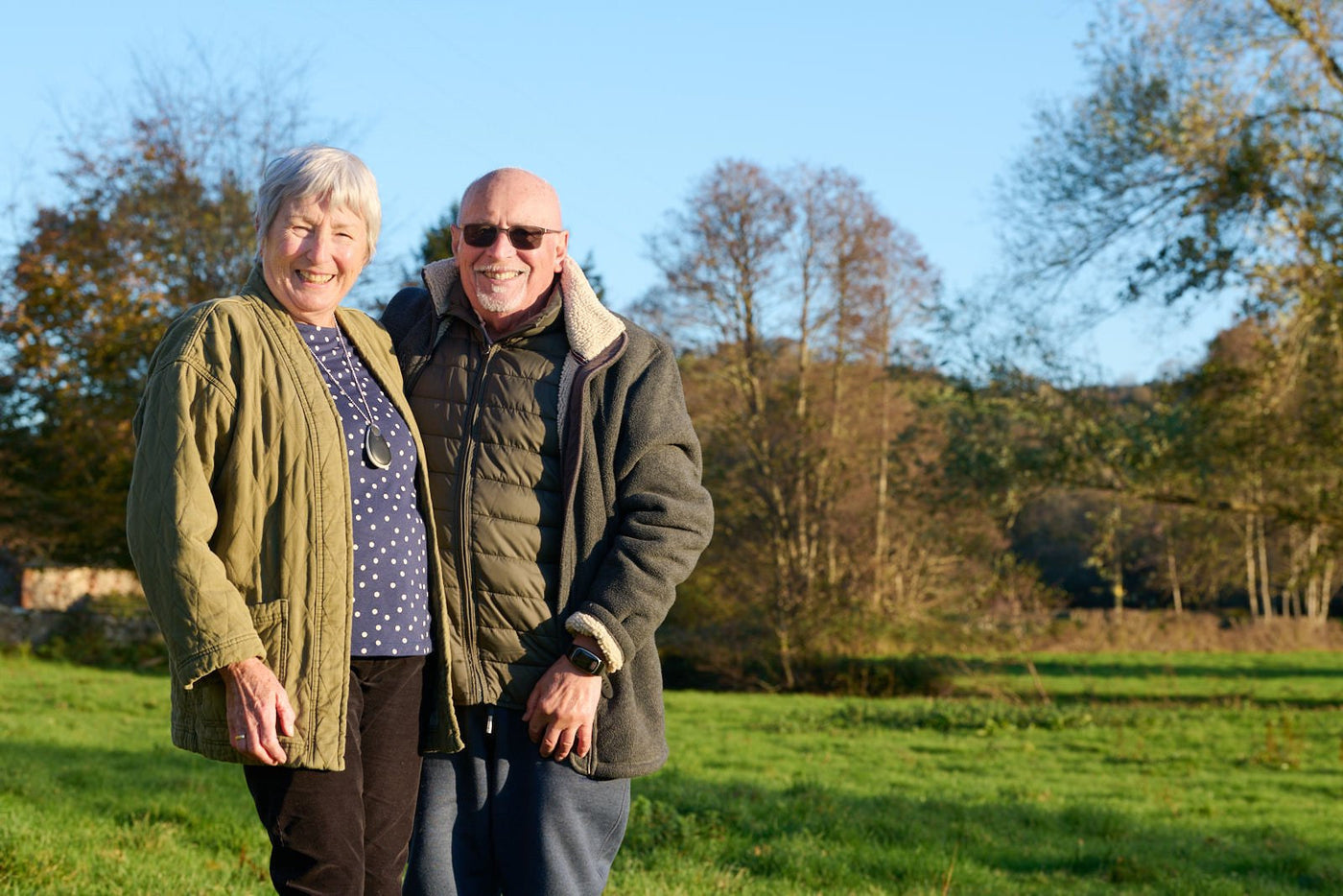 Elderly woman and man stood together outside wearing personal alarms