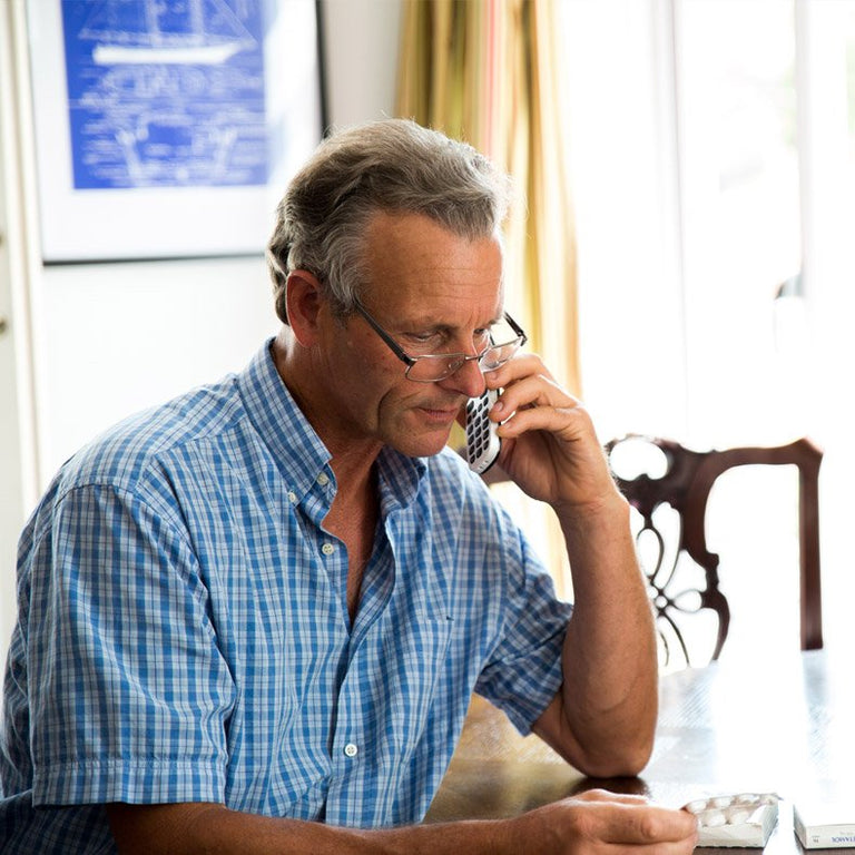 Man in a blue checkered shirt talking on a phone indoors