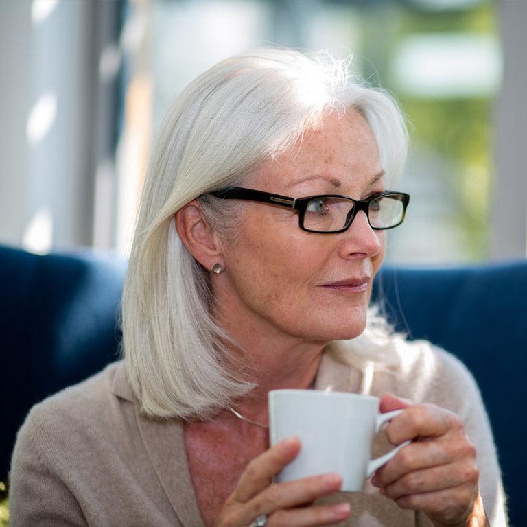 Senior woman with glasses holding a white mug indoors
