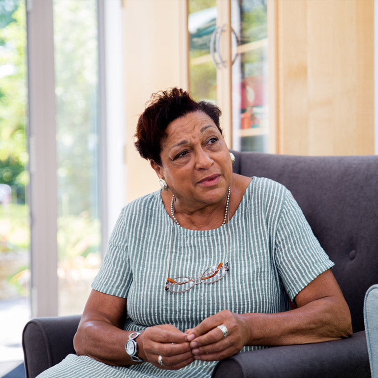 Elderly woman sitting on a couch in a room with large windows